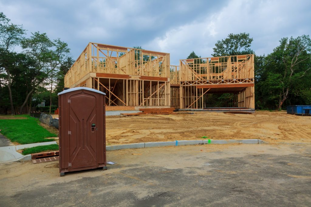Portable restroom on a new structure near a new house under construction.